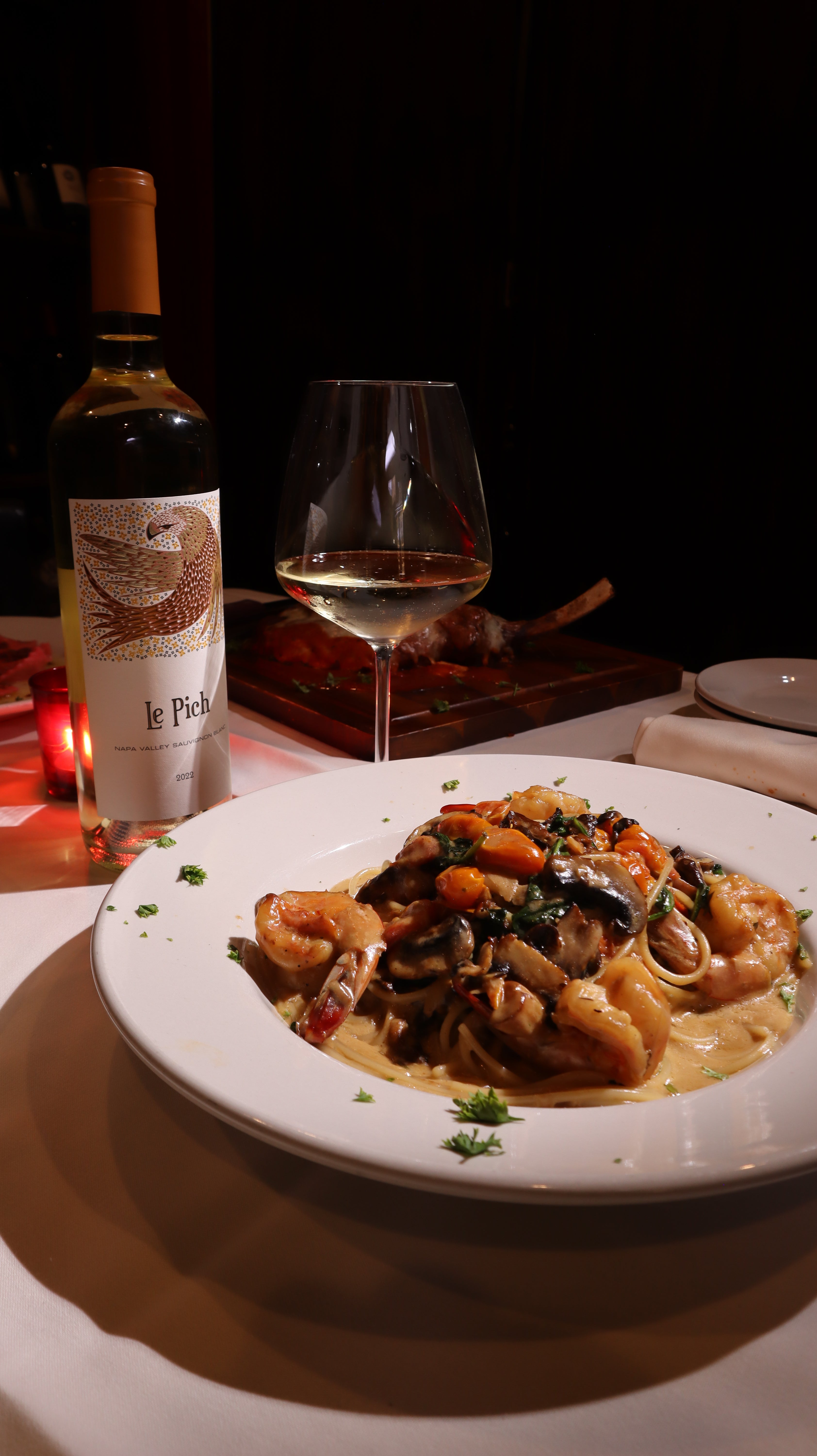 Plate of food with a glass of red wine and a bottle on a dark surface