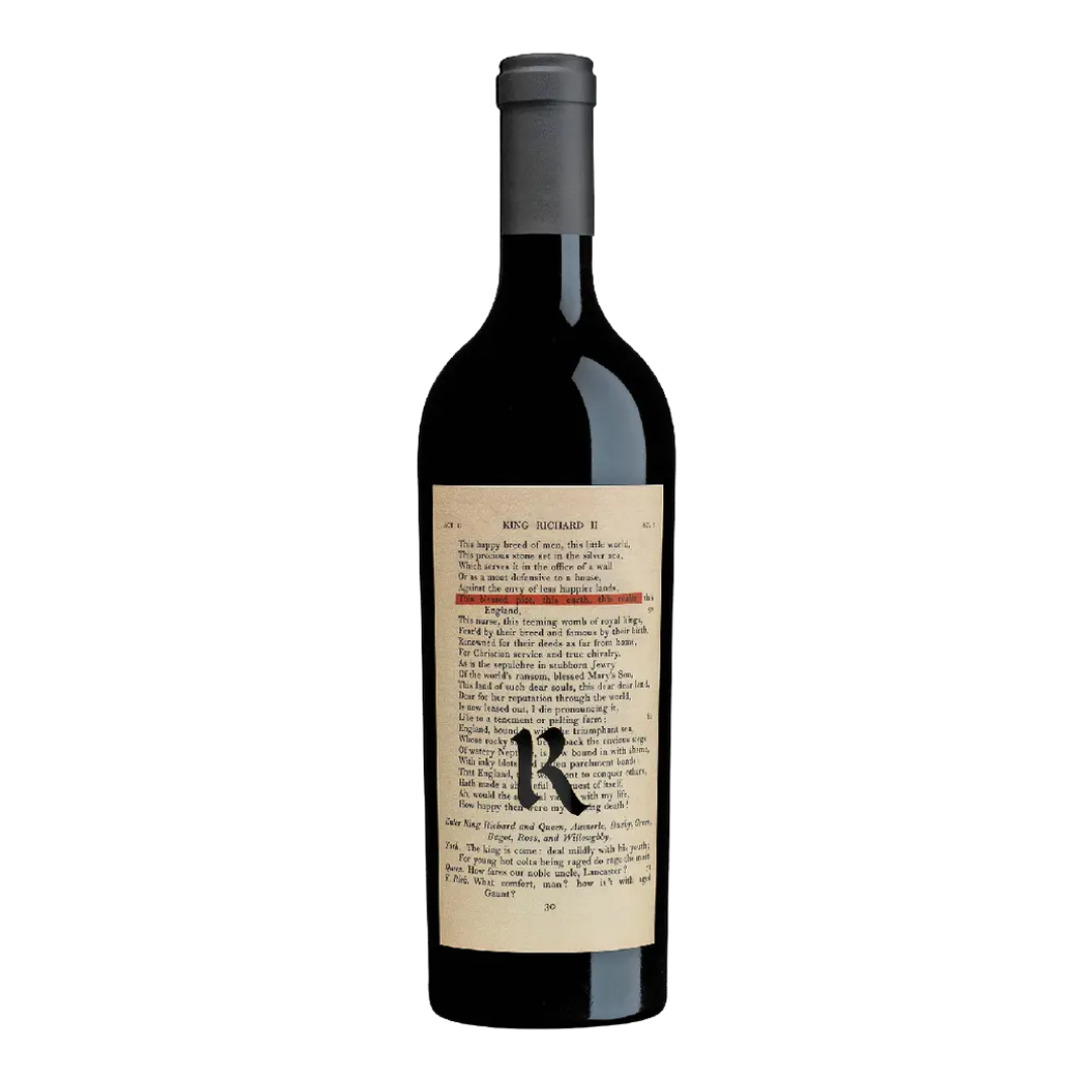 A bottle of Realm Cellars The Bard with a dark glass body and a cream label designed like a printed book page featuring text and a large letter “R,” set against a black background.